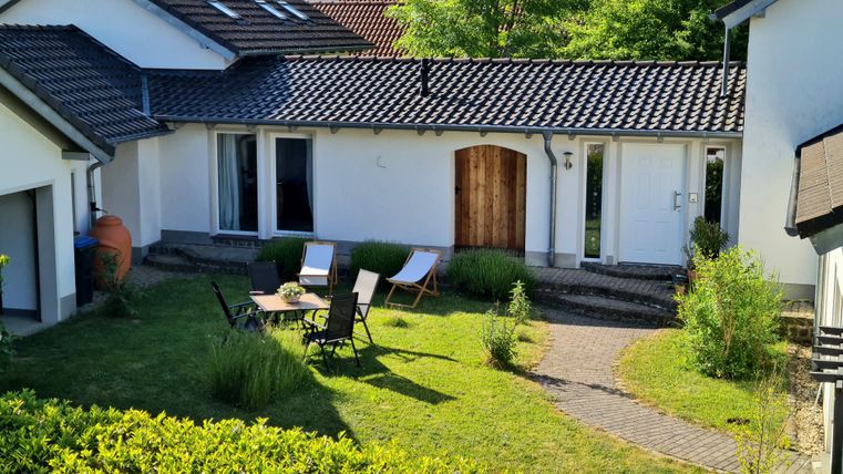 Ein schöner Gartenbereich mit einem kleinen Sitzplatz und einer Holztür. Umgeben von gepflegten Pflanzen und einem gemütlichen Ambiente.