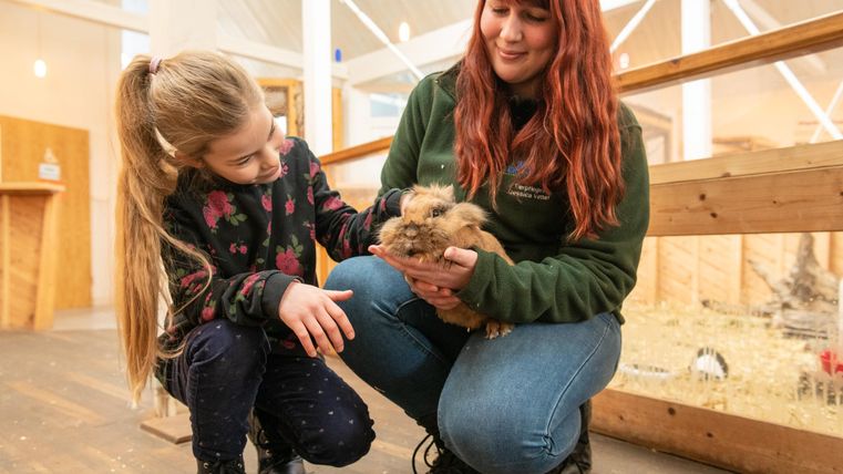 Een meisje en een vrouw houden een konijn in een dierenpark. Beiden glimlachen en tonen vreugde bij het omgaan met het dier.