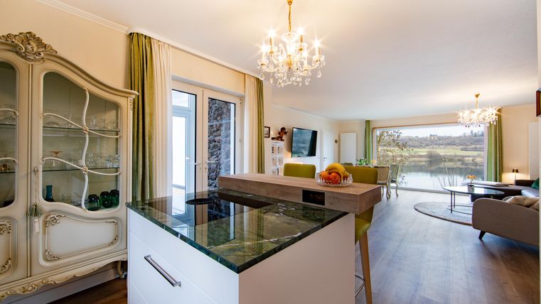 Eine moderne Küche mit einer eleganten Kochinsel und einem offenen Wohnbereich. Große Fenster bieten einen Blick auf die Natur und sorgen für viel Licht.