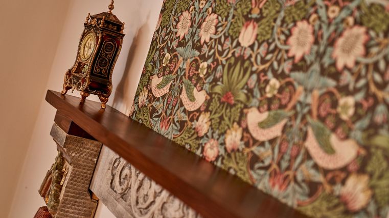 An elegant fireplace with a decorative wooden shelf. In the background, an ornate ornament and an antique clock are visible.