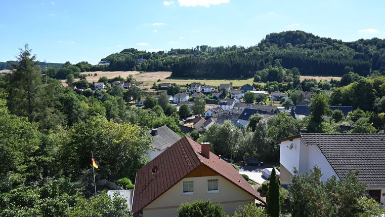 Een schilderachtig landschap met veel huizen en weelderig groen. Op de achtergrond zijn zachte heuvels en een heldere blauwe lucht te zien.
