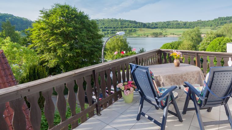 Ein schöner Balkon mit Blick auf einen See und grüne Hügel. Der Tisch ist gemütlich gedeckt, ideal für eine entspannte Zeit im Freien.