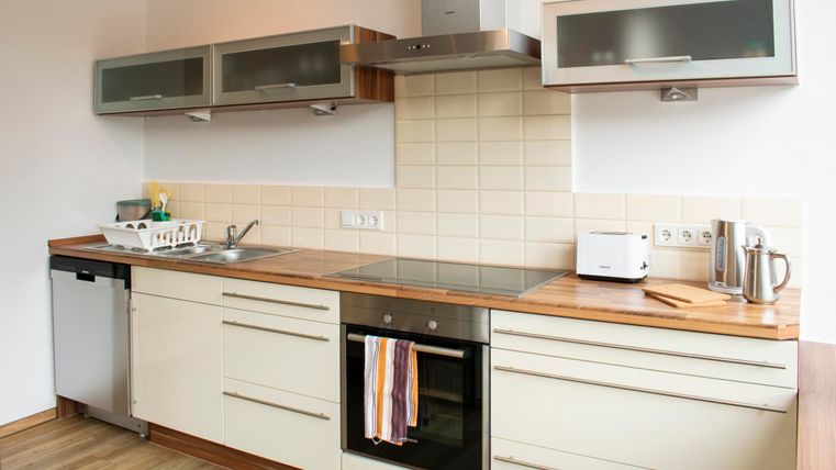 Eine moderne Küche mit hellen Schränken und einem Holzarbeitsplatz. Sie ist gut ausgestattet mit einem Herd, einem Kühlschrank und kleinen Küchengeräten.