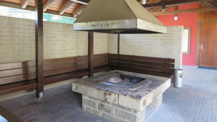 A barbecue area under a covered space with wooden benches. The grill is made of stone and has a large, slanted exhaust chimney.