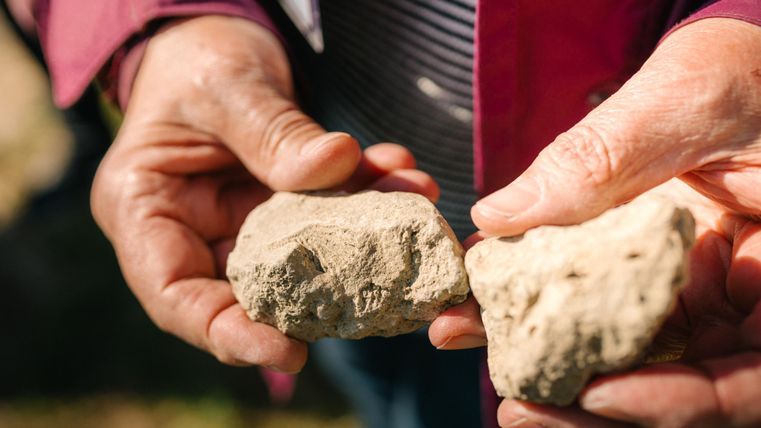 A person is holding two heavy stones in their hands. The stones are irregularly shaped and show different textures.