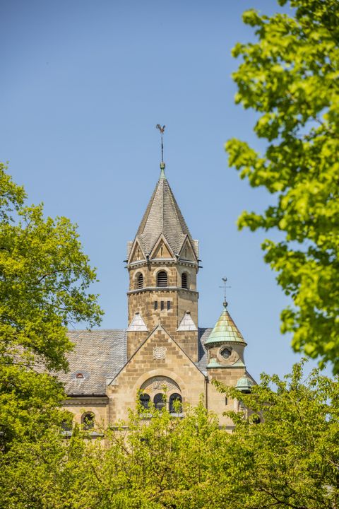 Kirchturm der Erlöserkapelle in Mirbach, umgeben von grünen Bäumen und blauem Himmel.