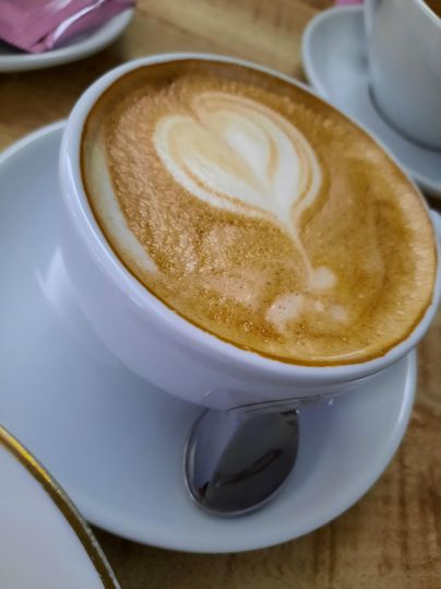 Eine Tasse Kaffee mit schöner Milchcreme, die ein Herzmuster zeigt. Der Becher steht auf einem kleinen Unterteller.