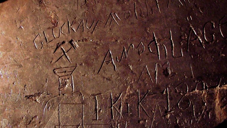 A stone surface with carved letters and symbols. The engravings appear to be historical and mysterious.