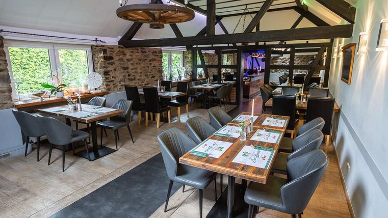 A modern restaurant with wooden beams and elegant tables. The decor is bright and inviting, with large windows that let in plenty of light.