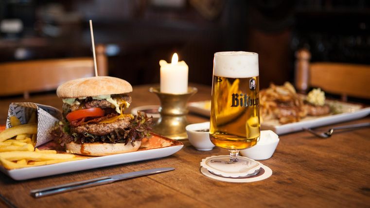 Ein leckerer Hamburger mit Pommes frites und einem Glas Bier auf einem Tisch. Eine Kerze sorgt für eine gemütliche Atmosphäre.