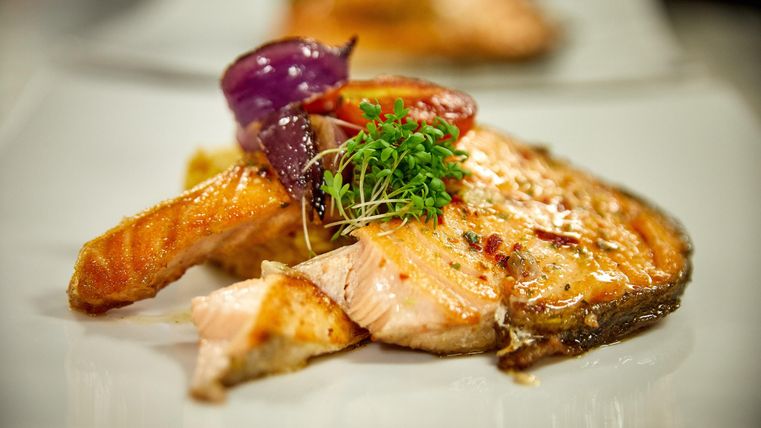 Ein köstliches Lachsgericht auf einem weißen Teller, garniert mit roten Zwiebeln und frischen Kräutern. Die speißen scheinen perfekt gegrillt und appetitlich anzusehen.