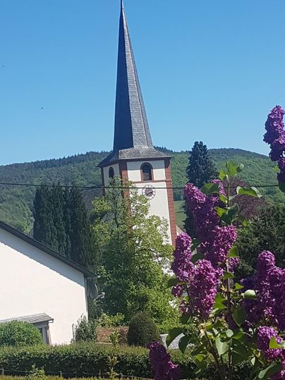 Eine Kirche mit spitzem Turm steht in einer malerischen Landschaft. Bunte Blumen blühen im Vordergrund.