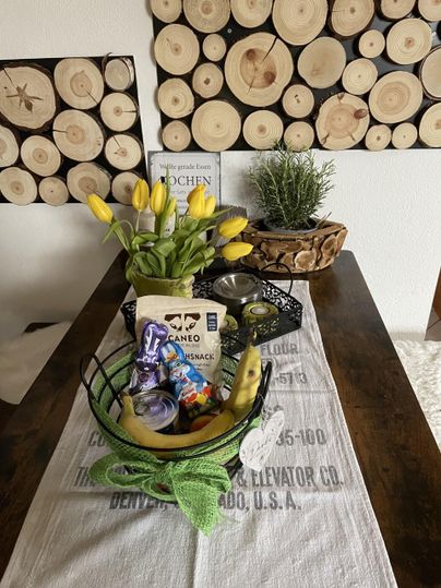 Een tafel met een decoratie van gele tulpen en een mand vol snacks. Op de achtergrond zijn houten schijven aan de muur te zien.
