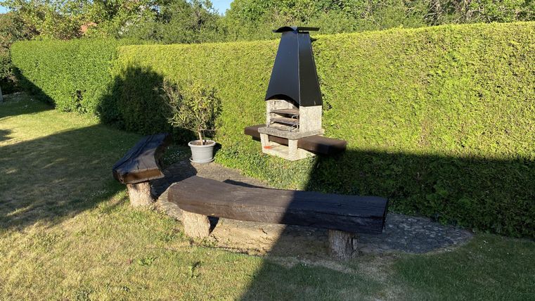 Ein gepflegter Garten mit einer grünen Hecke und einem Grill. Es gibt zwei Bänke aus Holz, die zum Entspannen einladen.