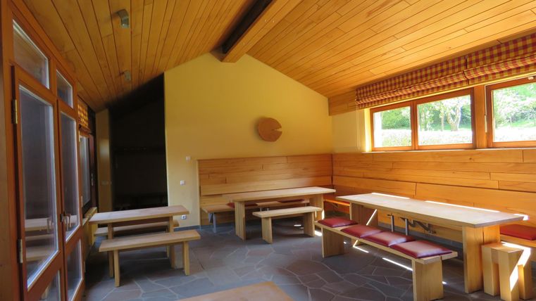A cozy room with wooden walls and benches. The large windows offer a view of the green surroundings.