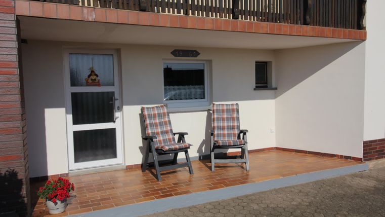 Een uitnodigende entree met twee comfortabele tuinstoelen. Een bloeiende plant staat naast de deur.