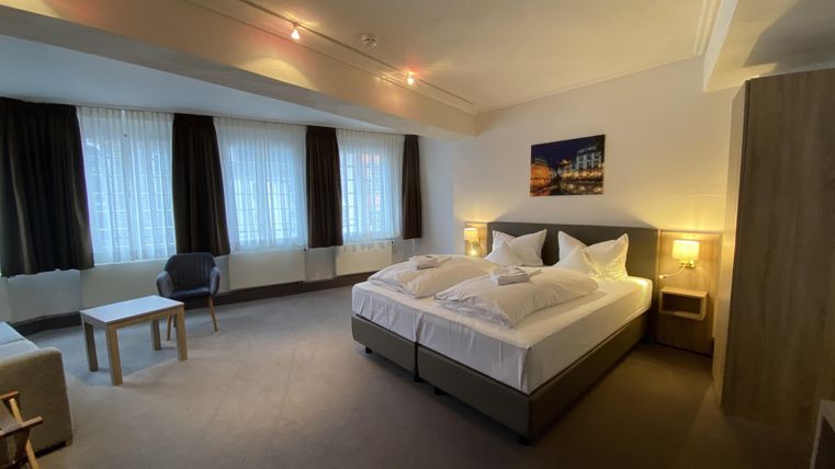 Ein modernes Schlafzimmer mit zwei Betten und sanfter Beleuchtung. Der Raum ist mit einem Tisch, einem Stuhl und großen Fenstern ausgestattet.