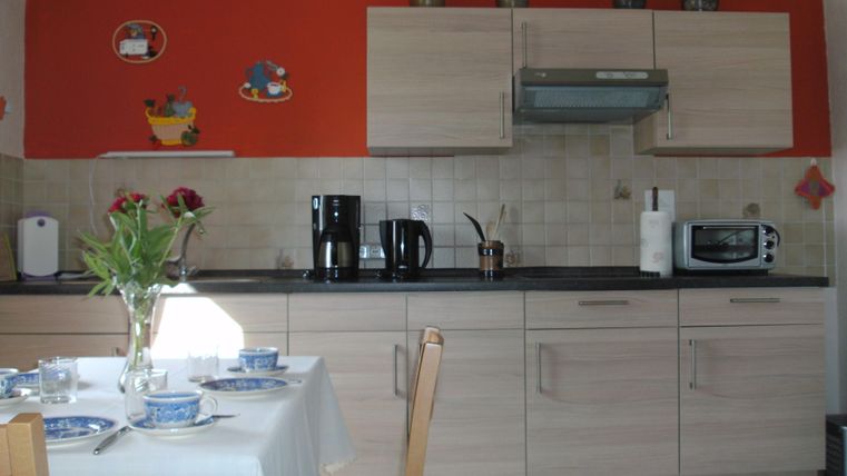 Eine moderne Küche mit Holzschränken und einem roten Akzent. Auf dem Tisch sind Geschirr und eine Vase mit Blumen dekoriert.