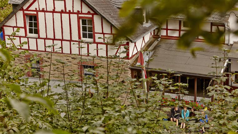 A historical building with red timber framing in a green setting. In the foreground are people relaxing and enjoying nature.