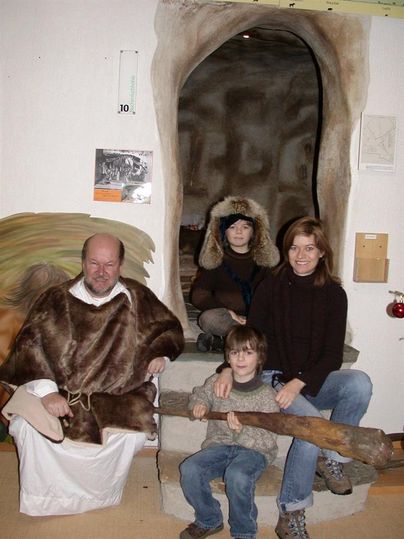 Gruppe im Museum vor einer Höhlenkulisse. Ein Mann in Fellkostüm, zwei Kinder und eine Frau posieren. Ein Kind hält einen großen Stock.