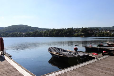 Ein ruhiger See unter klarem Himmel mit sanften Hügeln im Hintergrund. Ein kleines Boot liegt an einem Steg.