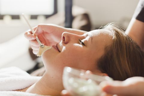 Eine Frau erhält eine Gesichtsbehandlung in einem Wellness-Salon. Ein Mitarbeiter trägt sanft eine Maske auf ihr Gesicht auf.