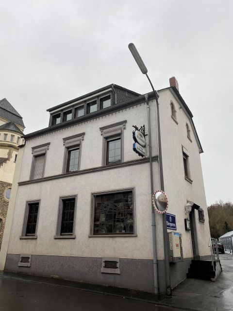 Een meerlaagse, lichte gebouw op een straathoek. De lucht is bewolkt en het ziet eruit als regen.