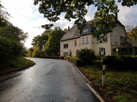 Ein kurvenreicher Weg führt vorbei an einem großen, schönen Haus. Die Umgebung ist grün und es ist bewölkt.