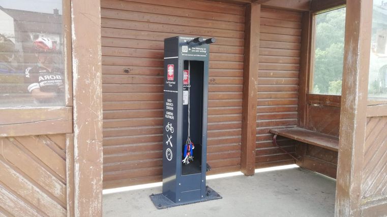 A bicycle workshop is located at a bus stop. In the background, wooden paneling is visible.