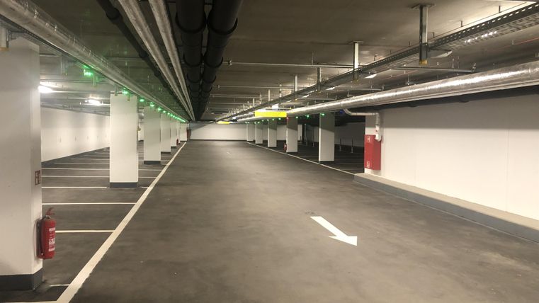 An empty underground parking garage with many parking spaces. The walls are light-colored and the lighting is even.