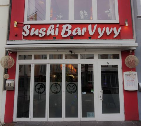 Ein einladendes Restaurant mit roter Fassade und großen Fenstern. Das Schild zeigt den Namen "Sushi Bar Vyvy" in auffälligen Buchstaben.