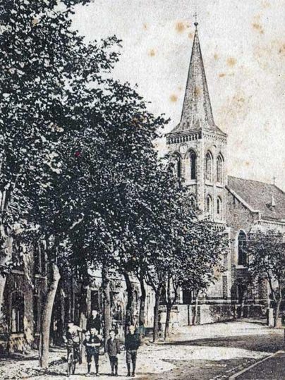 Eine alte Straße mit Bäumen und einem Kirchengebäude im Hintergrund. Mehrere Personen gehen in der Nähe der Kirche spazieren.