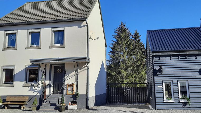 Ein modernes Haus mit einem klaren blauen Himmel im Hintergrund. Neben dem Haus steht ein zusätzliches Gebäude in dunkler Farbe.