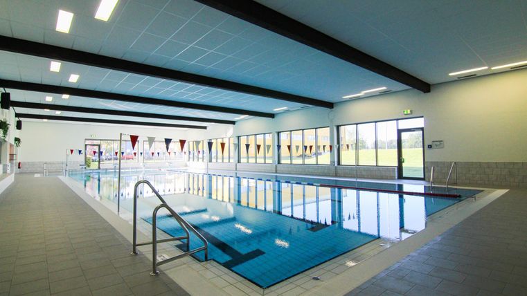 Een modern zwembad met helderblauw water. De grote ramen zorgen voor veel daglicht in de ruimte.