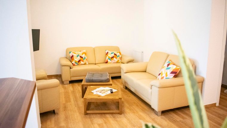 Ein gemütliches Wohnzimmer mit beigen Sofas und bunten Kissen. Der Holztisch in der Mitte ergänzt den modernen, einladenden Stil.