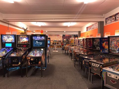 Ein Raum voller Flipperautomaten in verschiedenen Designs. Die Wände sind orange gestrichen, und es gibt genügend Platz für Spieler.