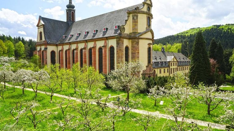An impressive church surrounded by blooming fruit trees and lush greenery. In the background, gentle hills and a clear sky are visible.