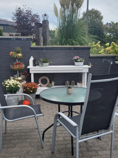 A cozy terrace with a round table and chairs. Colorful flowers in pots create an inviting atmosphere.