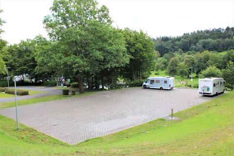 Ein ruhiger Wohnmobilstellplatz mit grünem Rasen und Bäumen. Zwei Wohnmobile stehen auf dem gepflasterten Boden.