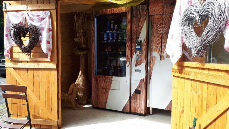 Ein rustikaler Holzstand mit einer Verkaufsautomaten und dekorativen Herzen. Die Atmosphäre ist einladend und gemütlich.