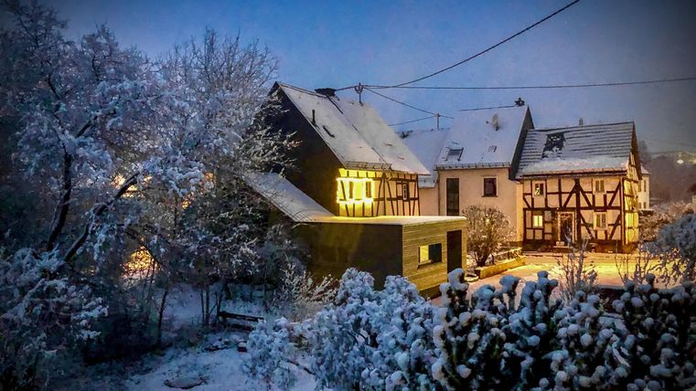 Ein verschneites Dorf im Abendlicht. Die beleuchteten Häuser strahlen Wärme in der kalten Winterlandschaft aus.