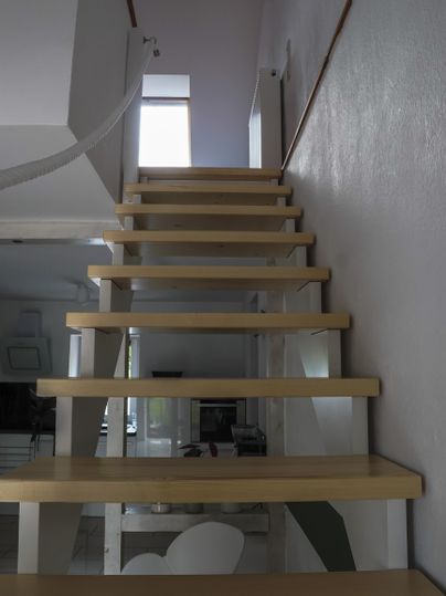 Eine moderne Treppe aus Holz mit einem klaren, minimalistischen Design. Im Hintergrund ist ein Fenster, das natürliches Licht hereinlässt.