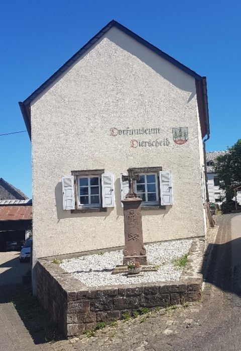 Een oud gebouw met twee ramen en een pomp ervoor. De gevel heeft de tekst "Dorfgemeenschap Dienersheim".