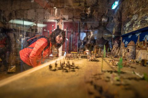 Eine Person in einem Museum betrachtet eine detailreiche Miniaturstadt. Im Hintergrund sind historische Exponate und Statuen zu sehen.