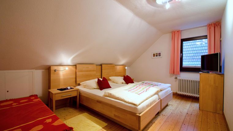 A cozy bedroom with two beds and light wooden furniture. There is a television and window curtains in soft colors.