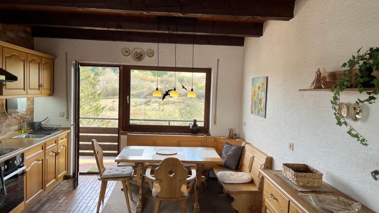 Eine gemütliche Küche mit Holzmöbeln und einem großen Esstisch. Durch die Fenster bietet sich ein schöner Blick ins Grüne.