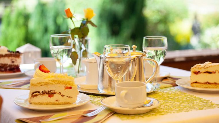 Ein schön gedeckter Tisch mit verschiedenen Kuchen und einer Teekanne. Auf dem Tisch stehen auch Gläser mit Wasser und eine kleine Blumenvase.