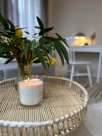 Een stijlvolle tafel met een kaars en een vaas met verse bloemen. Op de achtergrond is een lichte ruimte met een bureau zichtbaar.