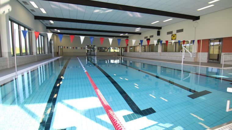 Een modern binnenzwembad met helderblauw water. Aan de rand van het bad zijn zwemboulevard en lichten bevestigd.