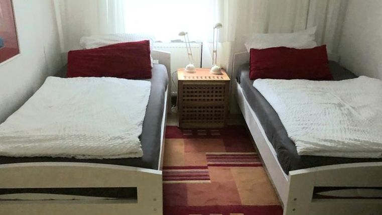 Ein gemütliches Schlafzimmer mit zwei Einzelbetten. Zwischen den Betten steht ein kleiner Tisch mit einer Lampe.